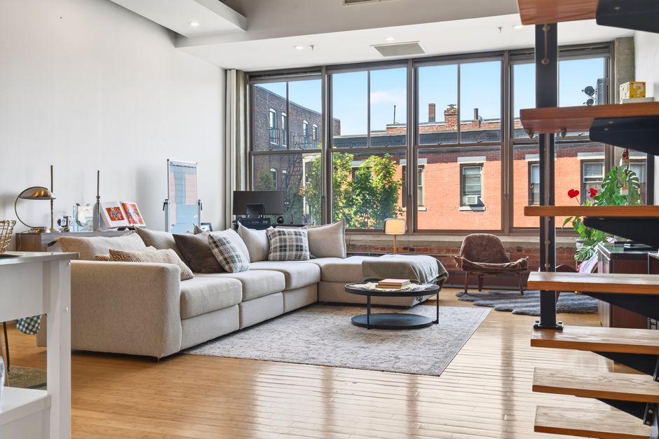 Open-plan loft living area with large windows, a sectional, and a dining table